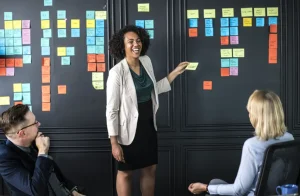 Frau präsentiert Ideen auf Haftnotizen an Wand, Teammeeting