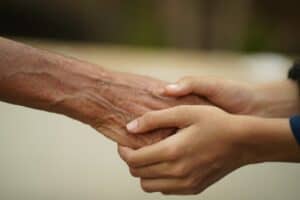 Nahaufnahme von einer jungen Hand, die eine ältere Hand hält, symbolisiert Pflege und Unterstützu.