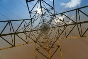 Hochspannungsleitung und Strommast aus der Perspektive nach oben, mit blauer Himmel und Sonnenlicht.