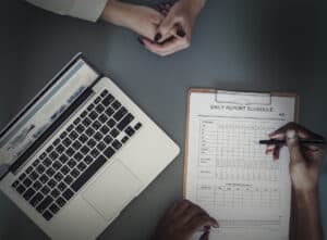 Person schreibt auf Wochenplan neben Laptop, Büroarbeit, Organisation, Planung.